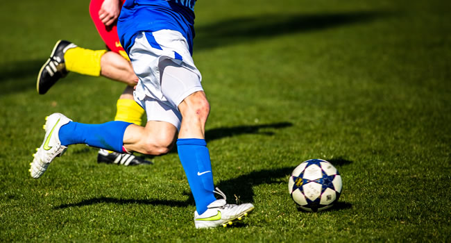 Football player dribbling with the ball under pressure from a defender during open play