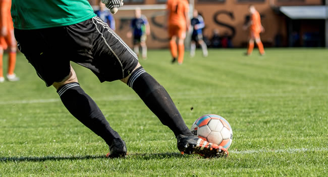 Goalkeeper striking a goal kick with close-up focus on ball contact and lower body movement