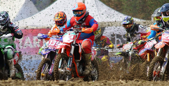 Group of motocross riders accelerating from the start line with mud spraying on an off-road track