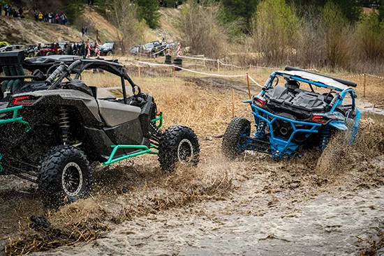 Two ATV riders racing on a muddy off-road track with water splashes, illustrating high-risk motorsport activity