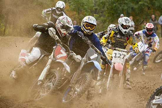 Pack of motocross riders racing closely on a dirt track, competing for position during a race